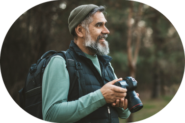 Older man smiles while holding a camera on a bird-watching hike