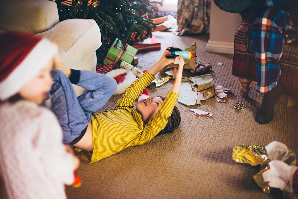 A boy plays with a new toy while surrounded by wrapping paper