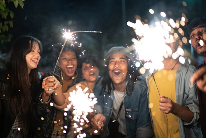 A group of young people smile and celebrate with sparklers