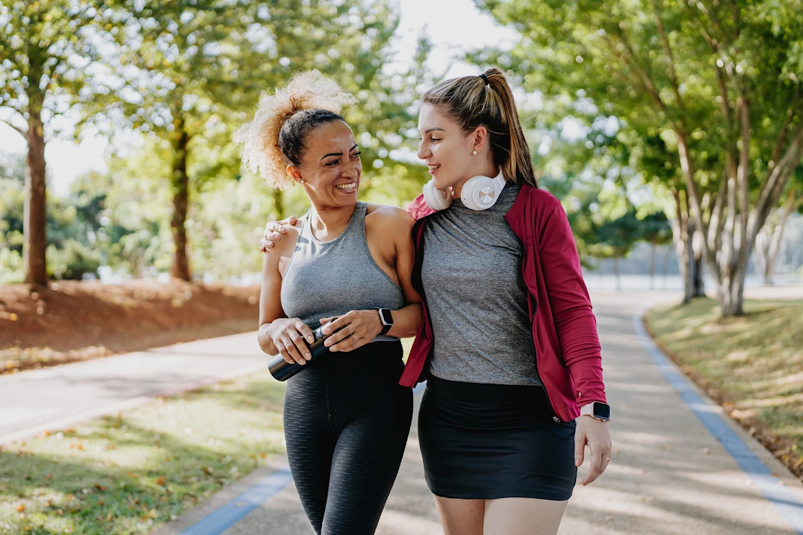 Two women in workout wear walk in the park.
